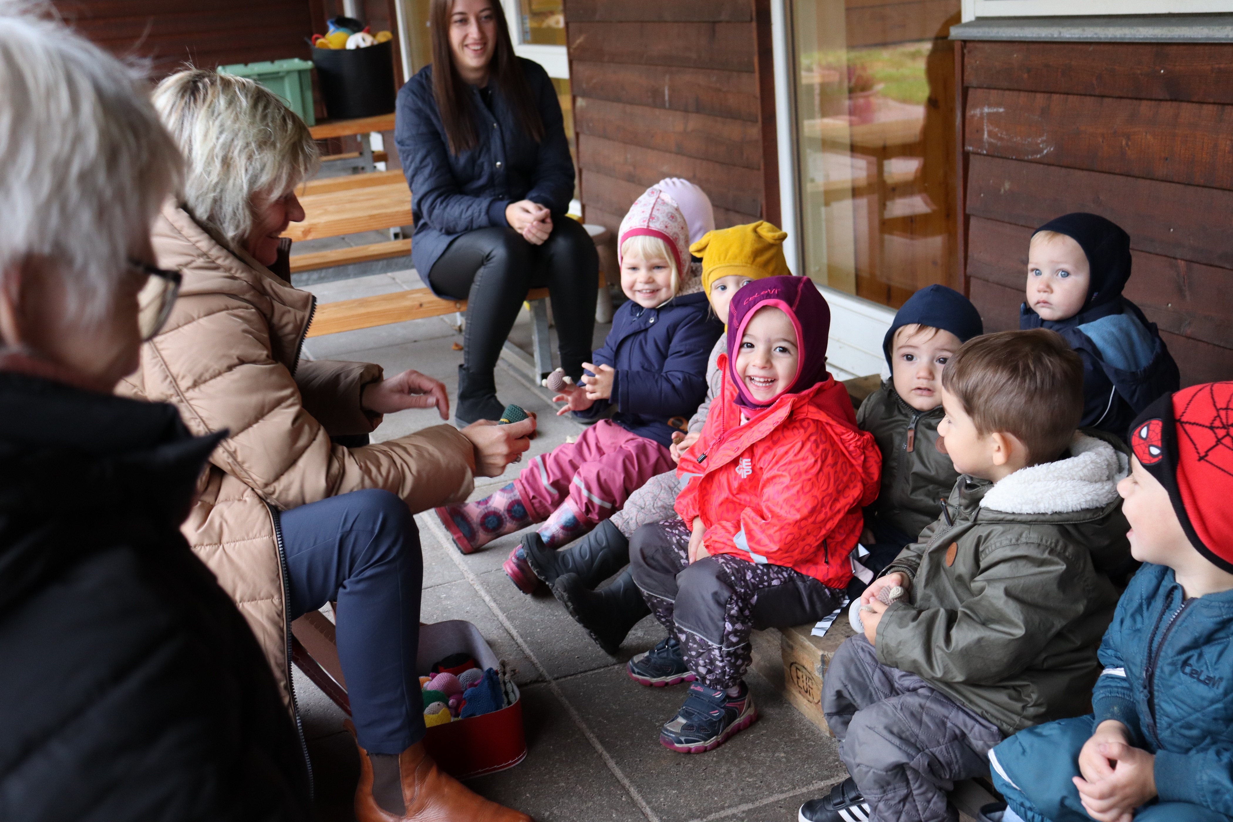 Vuggestue børn har samling udenfor med pædagoger omgivet omkring dem
