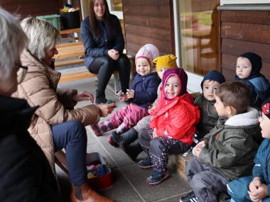 Vuggestue børn sidder udenfor med pædagoger omkring sig, og har en god samling